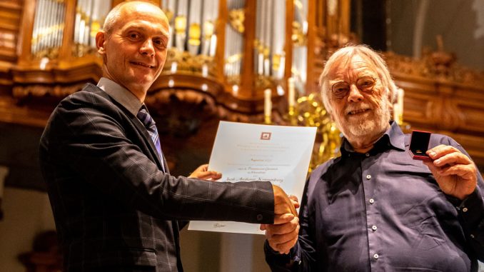 Jaap Kroonenburg (r) ontvangt de onderscheiding uit handen van kerkrentmeester Ko Heijboer